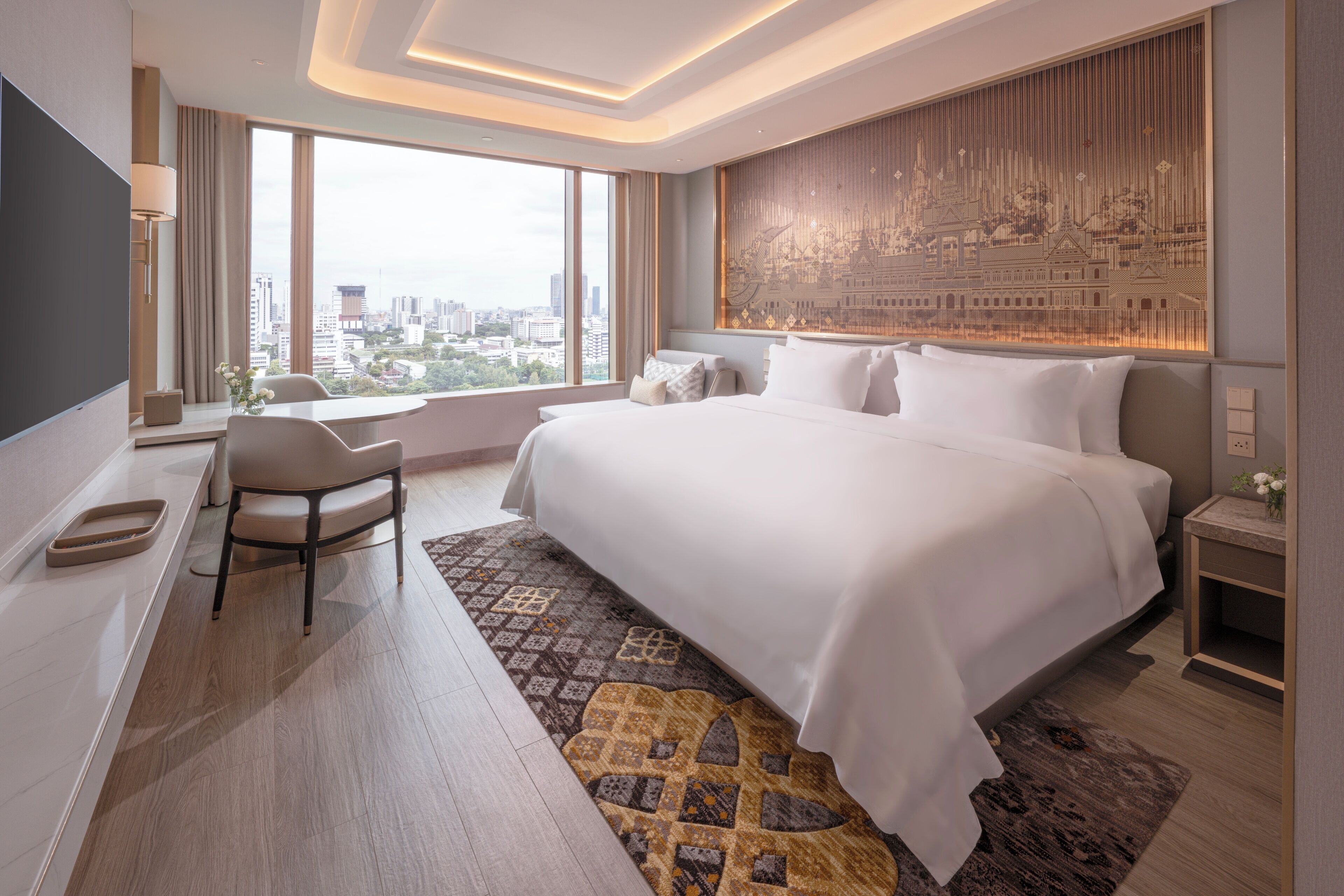 A modern hotel room with a large bed, a desk, and a view of the city.
