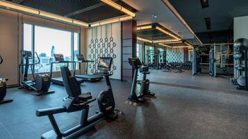 Un gimnasio moderno con máquinas de cardio, equipo de levantamiento de pesas y vistas a la ciudad a través de amplios ventanales.