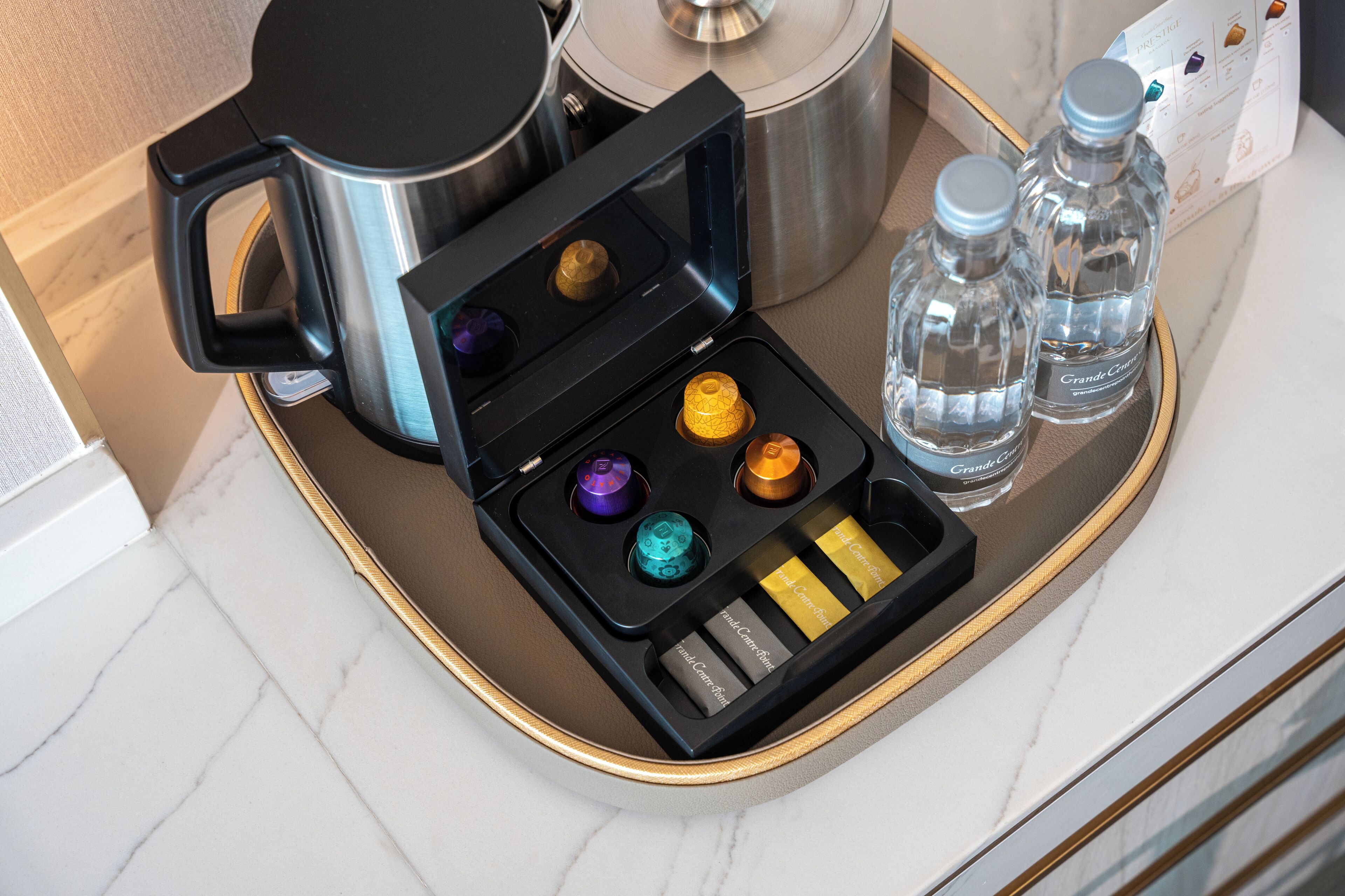A tray with a coffee maker, two water bottles, and a set of colorful drinkware.