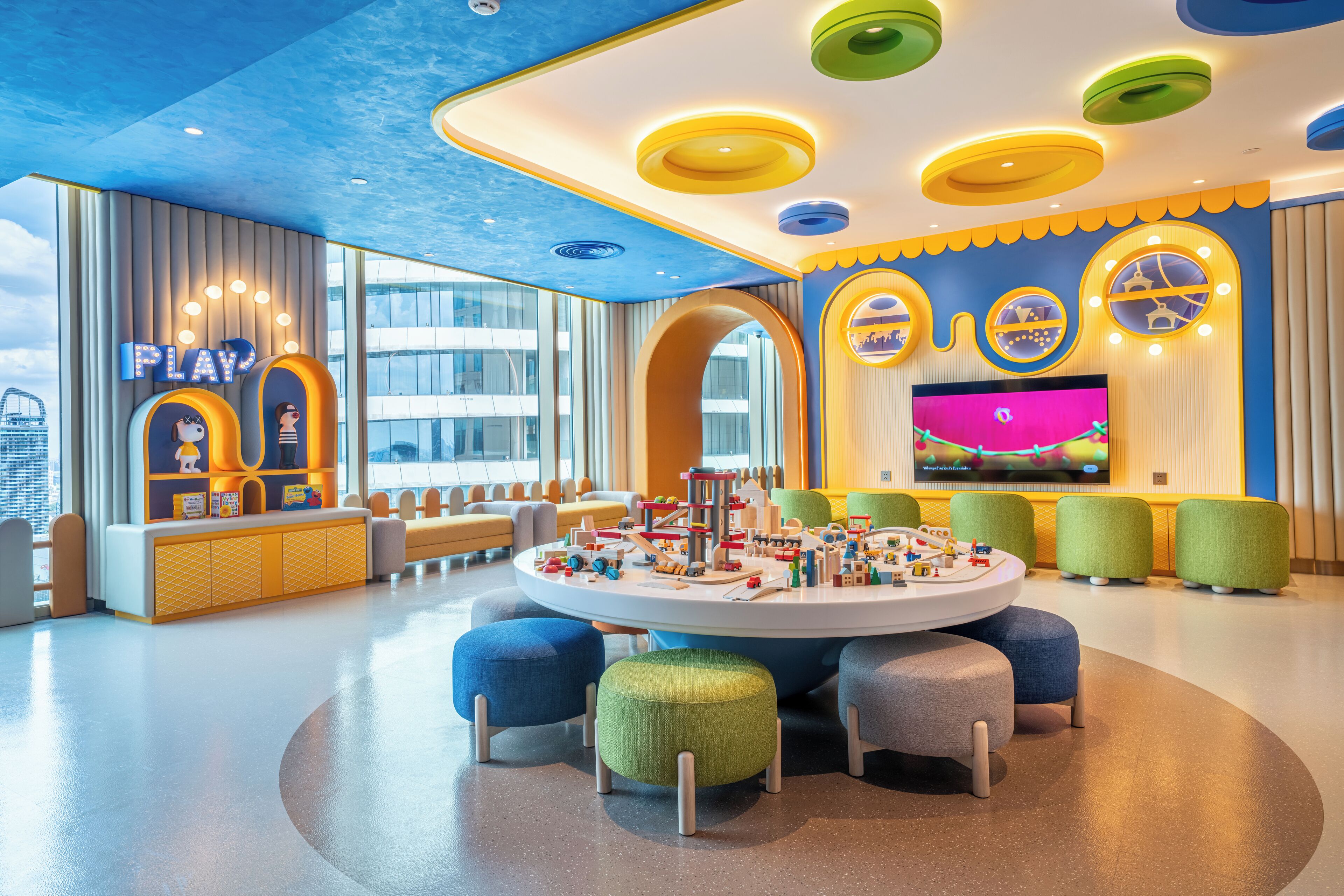 Ein hell erleuchteter Kinderspielbereich mit bunten Möbeln und einem großen Fernseher.
