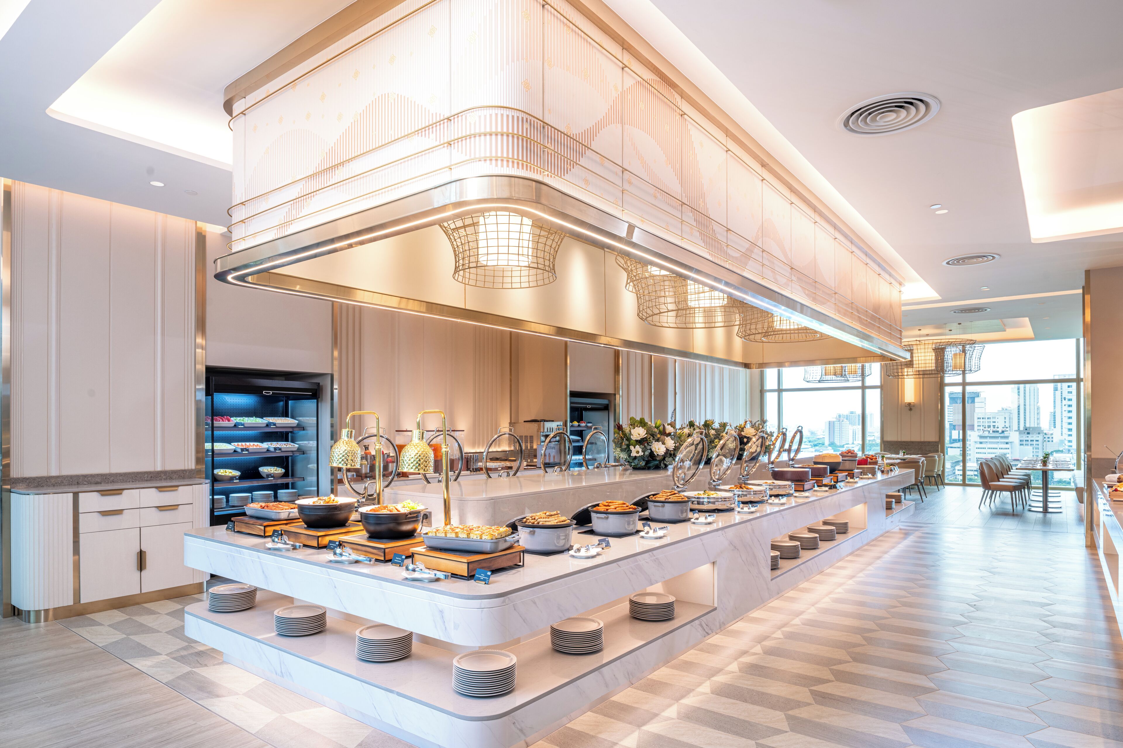 A modern hotel breakfast area with a long counter, buffet, and seating area.