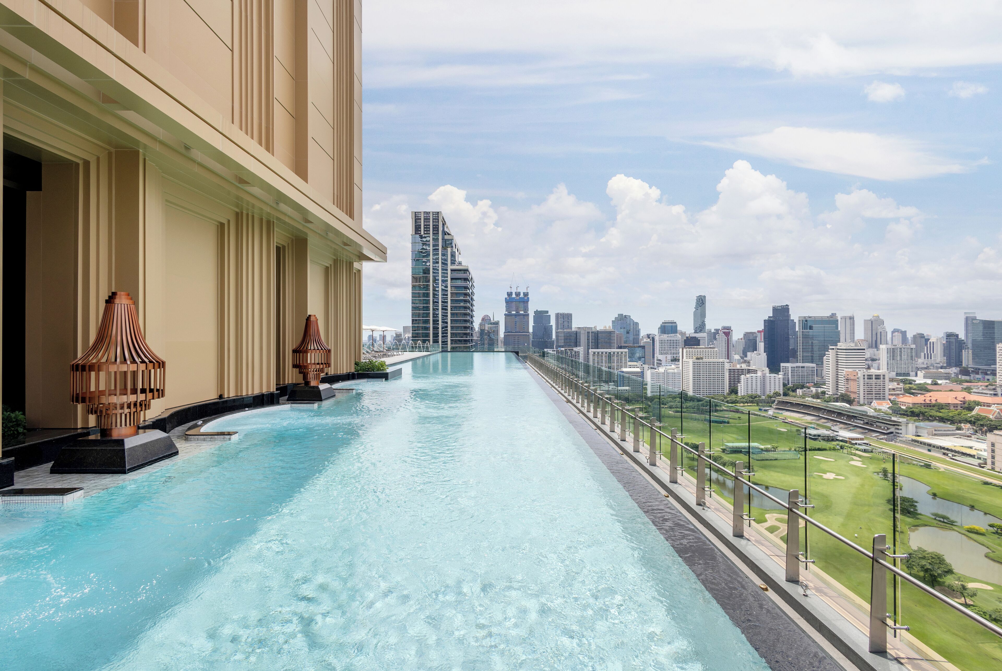 Una piscina infinita en la azotea con vistas a la ciudad, un edificio moderno y un cielo despejado.