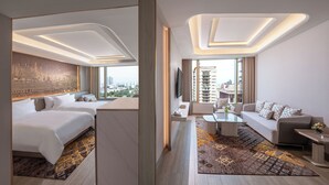Una moderna camera d'albergo con un letto grande, un divano, un tavolino da caffè e una TV. La stanza offre vista sulla città e un tappeto decorato.
