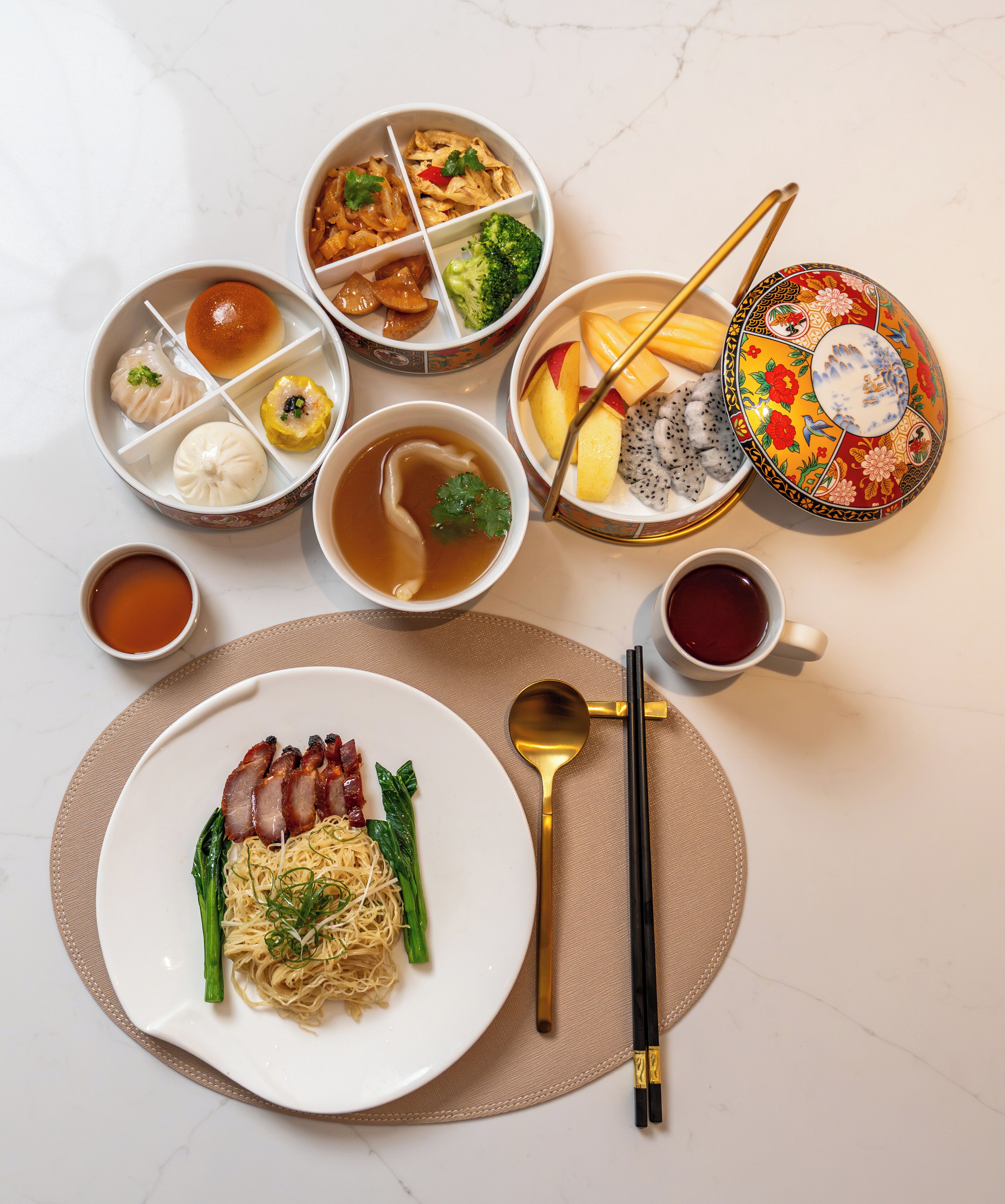 A variety of dishes including noodles, dumplings, and soup, arranged on a table with chopsticks and a spoon.