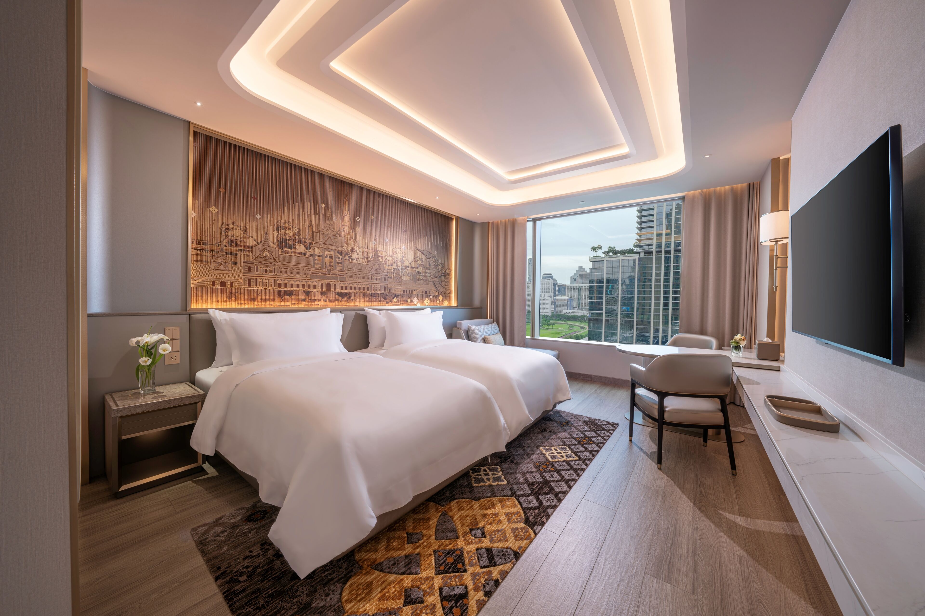 A modern hotel room with a large bed, a desk, a chair, and a TV.