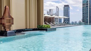 Area piscina moderna con una grande lampada di design, poltrone relax e vista sullo skyline della città.