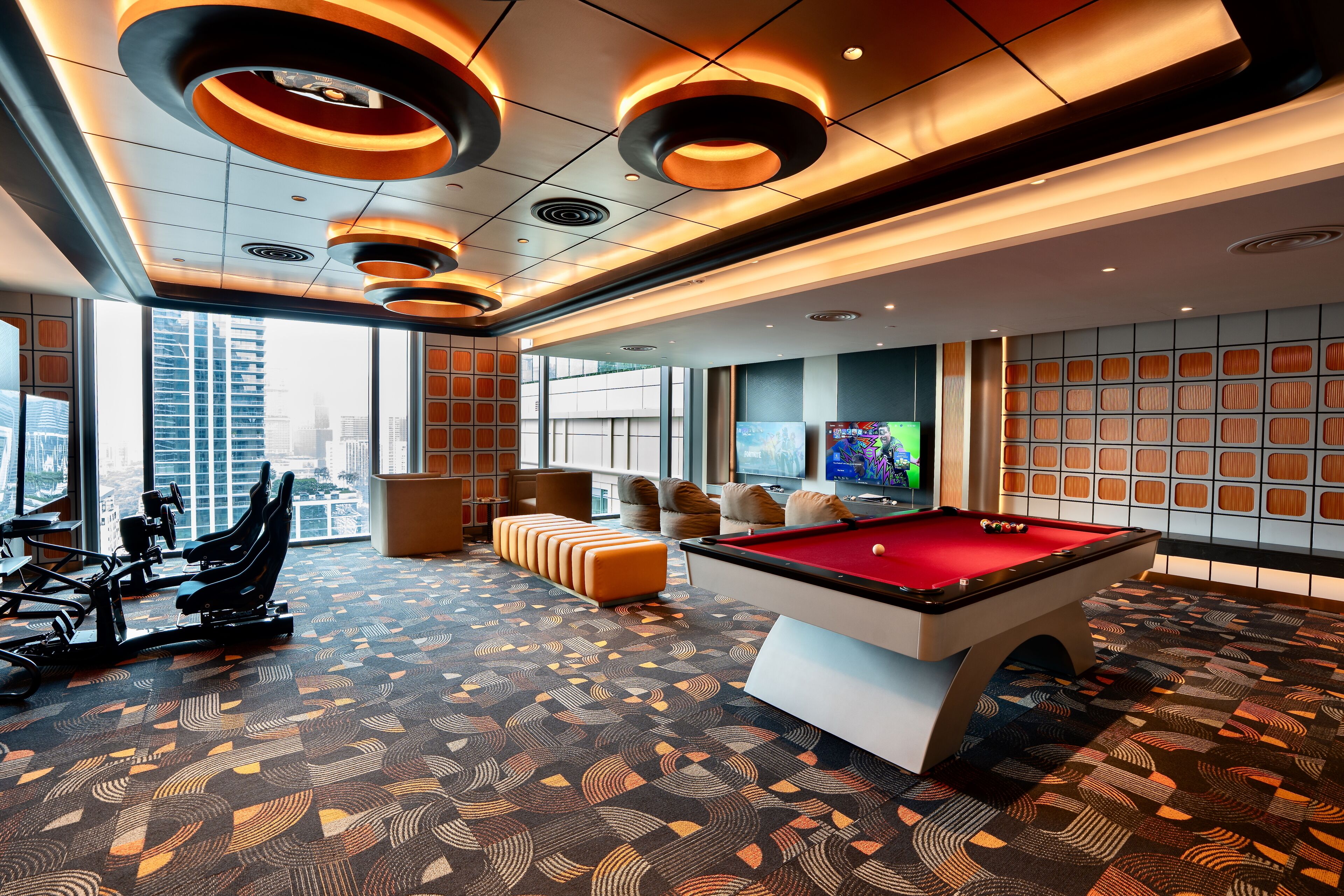 A modern indoor recreational area with a pool table, exercise equipment, and a seating area with a view of the city.