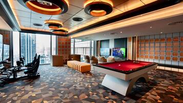 A modern indoor recreational area with a pool table, exercise equipment, and a seating area with a view of the city.