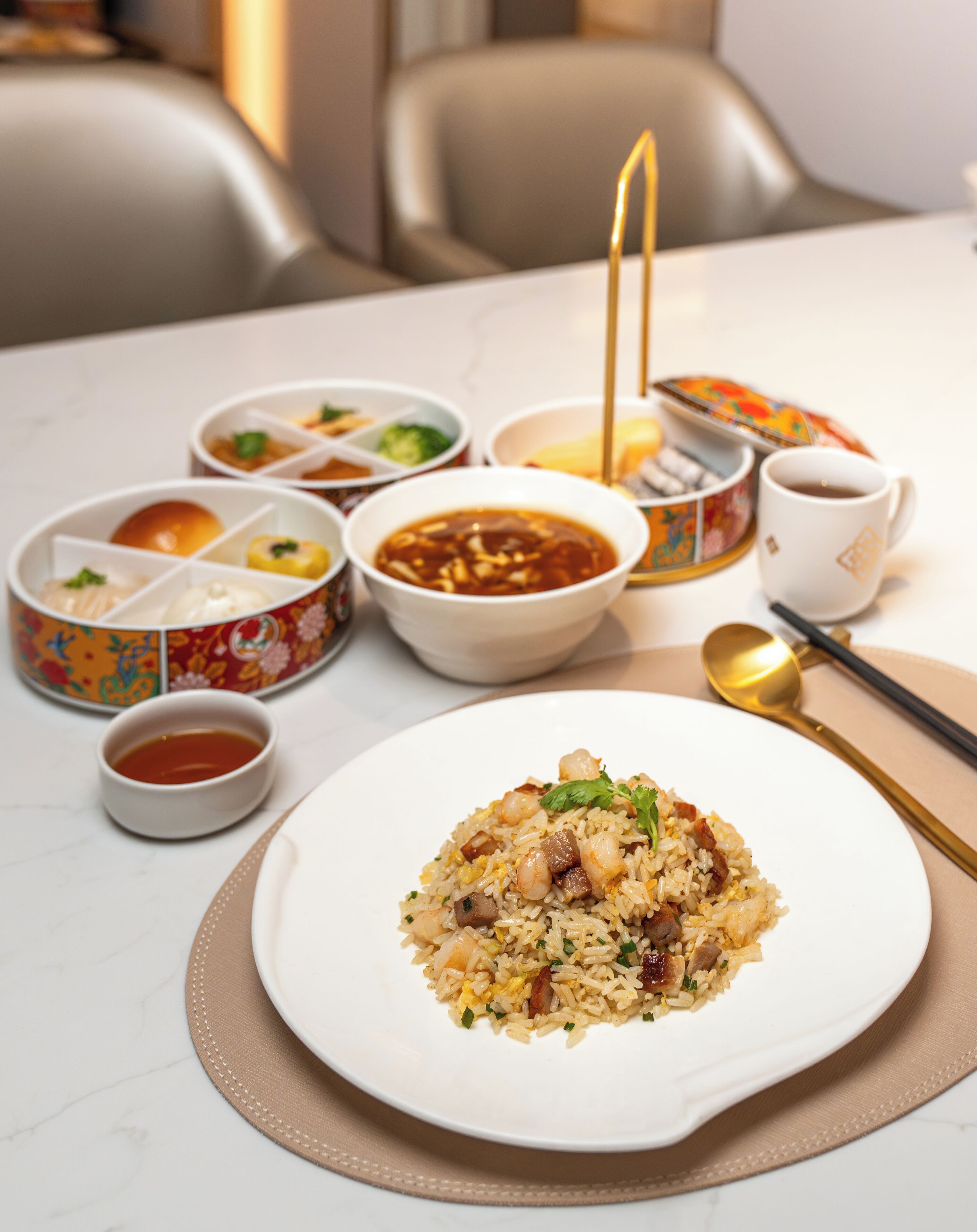 A table set with various dishes including a plate of fried rice, bowls of soup, and a teapot.