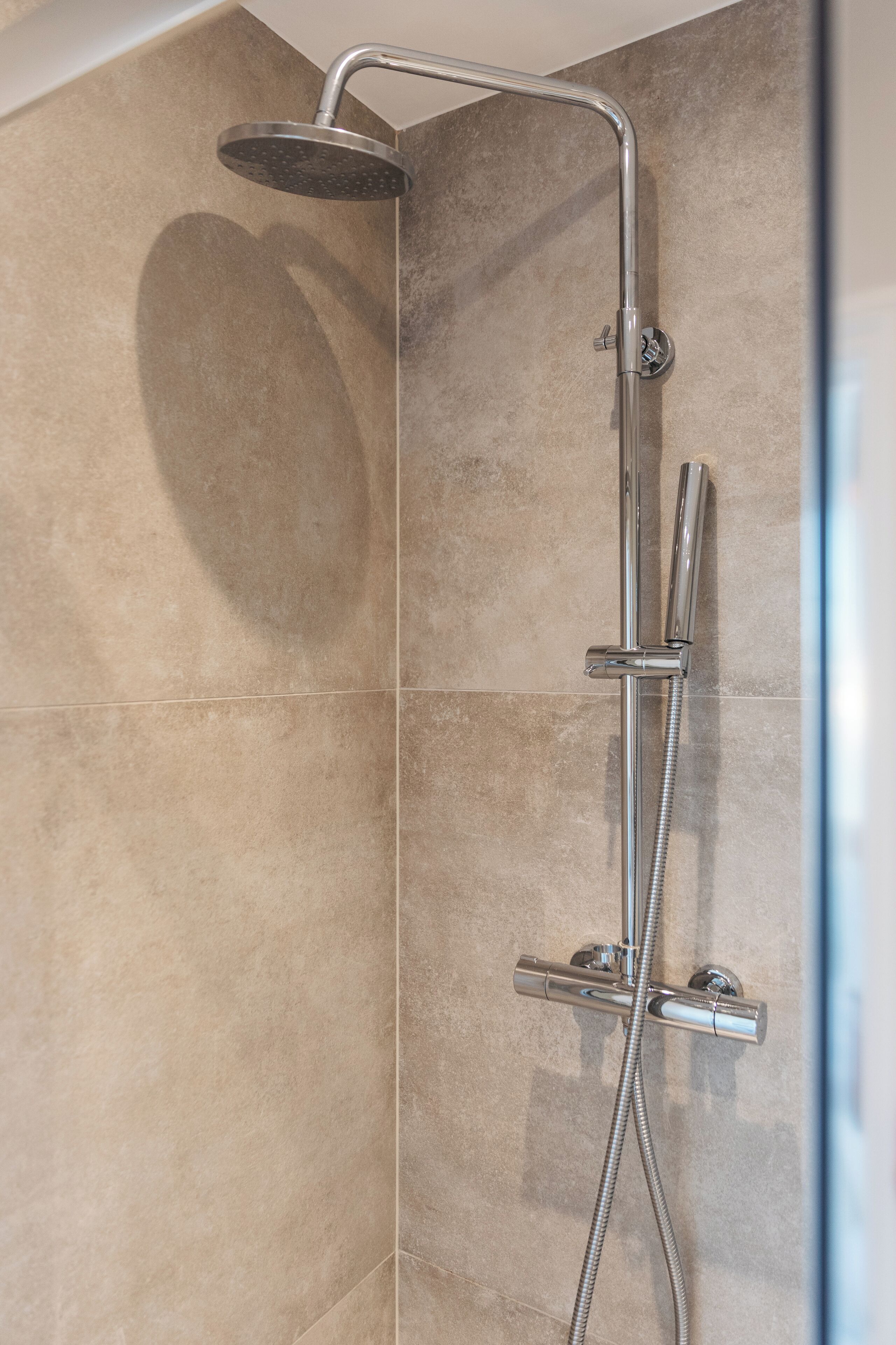 A shower with a handheld showerhead and a fixed wall-mounted showerhead, connected by a flexible hose.