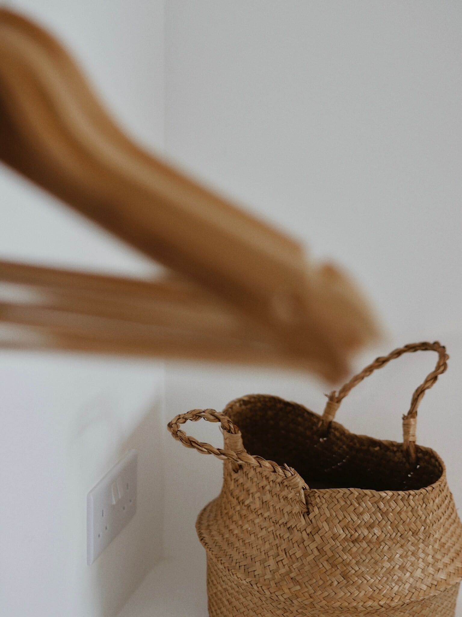 A woven basket with handles on a white wall, next to a power outlet.