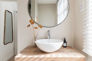 Un baño con un lavabo blanco, un espejo redondo y un mueble de tocador de madera.
