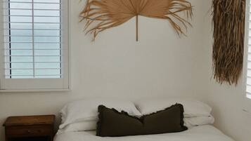 Un dormitorio con cama, mesita de noche, ventana con persianas y una decoración en la pared.