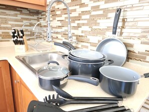 A kitchen with a stainless steel sink, a dish rack, and various pots and pans.