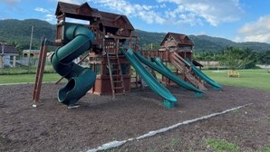 En lekplats med en lekställning i trä och en grön spiralrutschkana.