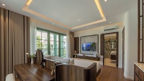 Une chambre d’hôtel moderne, dotée d’un bureau en bois, d’un canapé confortable, d’un téléviseur à écran plat et d’une salle de bain visible à travers une porte ouverte.