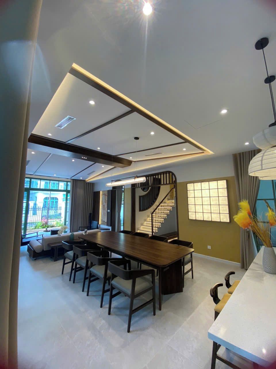 Un comedor moderno con una mesa larga y sillas, una escalera y ventanas amplias que dejan entrar luz natural.