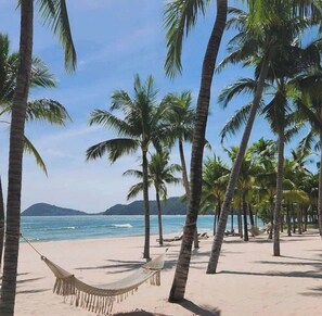 Ein Strand mit Palmen, einer Hängematte und Blick auf das Meer und ferne Berge.