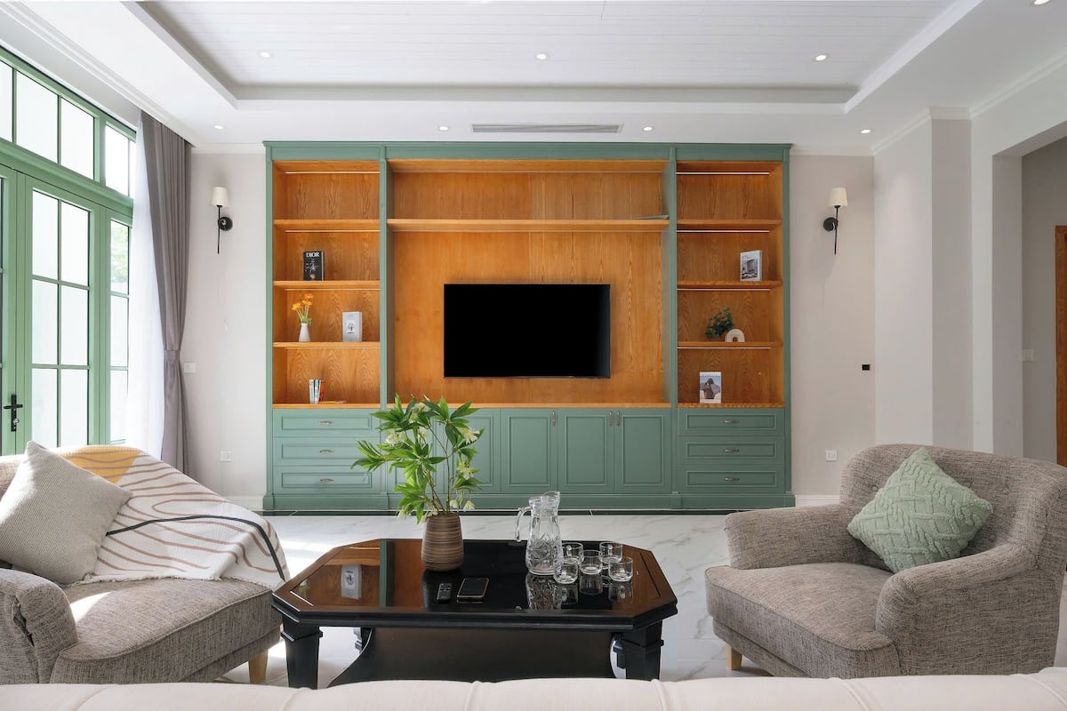 Een woonkamer met een grote televisie, groene kasten, twee banken en een salontafel.