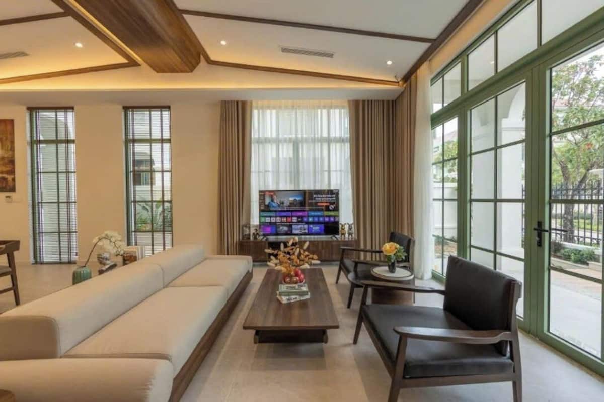 Een moderne woonkamer met een bank, salontafel, stoelen, een flatscreen televisie en grote ramen met gordijnen.