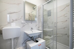 Een moderne badkamer met een marmeren wand, een wit wastafelmeubel, een toilet en een douchecabine met glazen wanden.