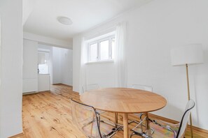 Een ruime kamer met een houten eettafel, transparante stoelen, een vloerlamp en een raam met witte gordijnen.