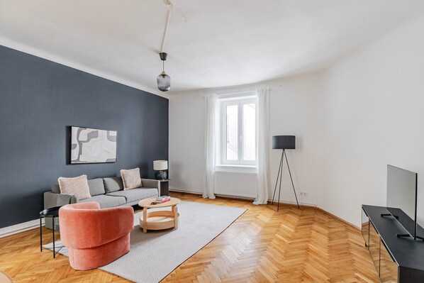 Een moderne woonkamer met een grijze bank, een roze poef, een ronde salontafel en een vloerlamp.