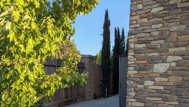 A paved pathway leading to a stone building with a metal gate, surrounded by trees and a wooden fence. - Suite #2 Full Private Studio - Brand New! (Clovis)