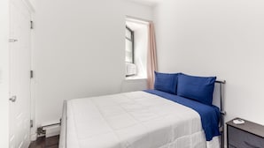 A bedroom with a bed, a nightstand, a window with a curtain, and a door.