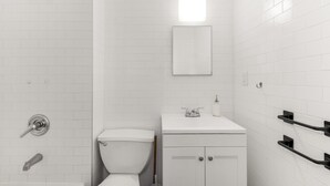 A modern bathroom with white tiles, a toilet, a sink with a mirror, and a shower area.