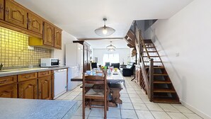 Une cuisine spacieuse avec des meubles de rangement en bois, une table à manger et un escalier menant à un autre niveau.