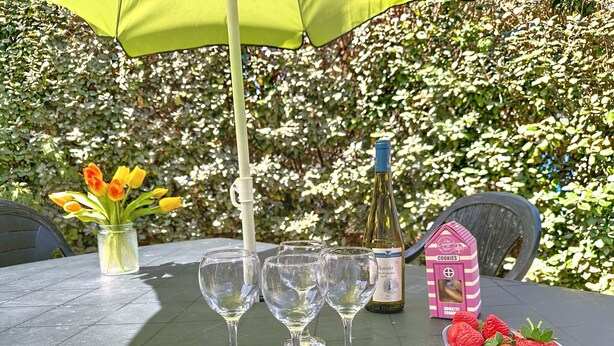 Une table avec quatre verres à vin, une bouteille de vin, un vase de fleurs et une boîte de biscuits.