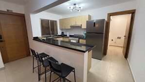 A modern kitchen with a central island, bar stools, a stainless steel refrigerator, and wooden cabinets.