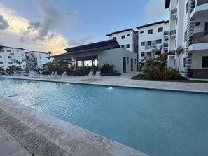 A modern hotel pool area with lounge chairs, a covered seating area, and a clear view of the pool.