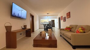 A modern living room with a flat-screen TV, a wooden coffee table, a sofa, and a dining area in the background.