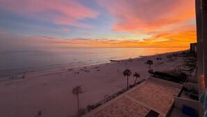 Blick auf einen Strand bei Sonnenuntergang, mit Palmen und einem Gebäude im Vordergrund.