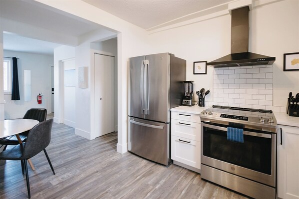 Een moderne keuken met roestvrijstalen apparatuur, een witte betegelde spatwand en een eethoek met een tafel en stoelen.