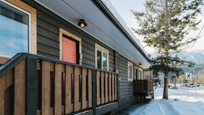 Una baita con veranda in legno, una porta rossa e montagne sullo sfondo.