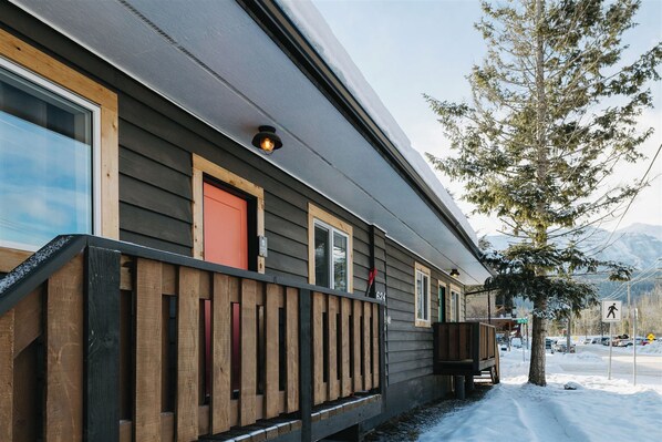 A cabin with a wooden deck, a red door, and a mountain backdrop.
