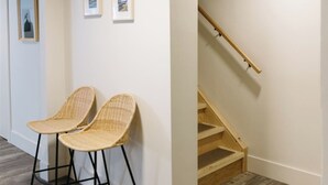 Un corridoio con due poltrone in vimini, una scala in legno e quadri appesi al muro.