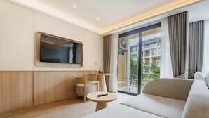 Una habitación de hotel moderna con una cama grande, un televisor montado en la pared, una pequeña mesa redonda y un balcón con vistas a la ciudad.