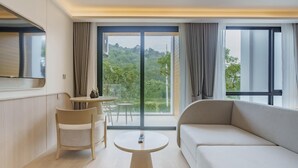 A modern hotel room with a large sofa, a round table, and a chair. There is a balcony with a view of greenery. - Sea Heaven Elegant Studio, Forrest View 2228 (Sakhu -  Thalang)