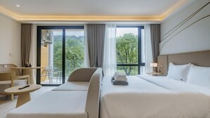 A hotel room with a large bed, a smaller bed, a sofa, a table, and a chair. There is a balcony with a view of trees and a building. - Sea Heaven Elegant Studio, Forrest View 2228 (Sakhu -  Thalang)