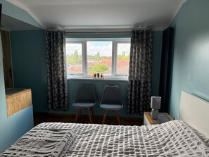 A bedroom with a bed, two chairs, a window with curtains, and a view of houses outside. - Private room with your own bathroom and shower (Birmingham)