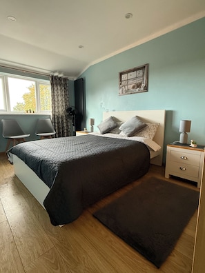 A bedroom with a large bed, bedside tables, a window with curtains, and a view of trees outside.