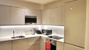Une cuisine compacte avec des meubles blancs, un four encastré, une plaque de cuisson, une bouilloire, un grille-pain et un four à micro-ondes.