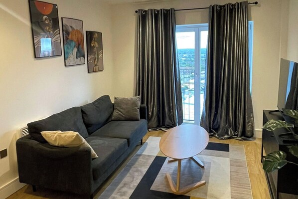 A modern living room with a dark grey sofa, a round coffee table, and a large window with dark curtains.