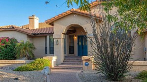 A two-story house with a beige facade, a blue door, and a small front garden with gravel and plants. - Glendale Paradise | Pool | Pickleball | Putt-Putt (Glendale)
