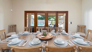 A dining area with a round table set for six, wooden chairs, and a view of a swimming pool through glass doors. - Glendale Paradise | Pool | Pickleball | Putt-Putt (Glendale)