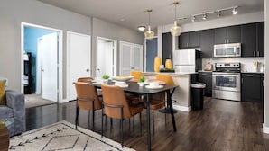 A modern kitchen with dark cabinets, stainless steel appliances, and a dining area with a table and chairs. - Stylish Resort Oasis: 5* Location, Pool, Gym, Pkg! (San Antonio)